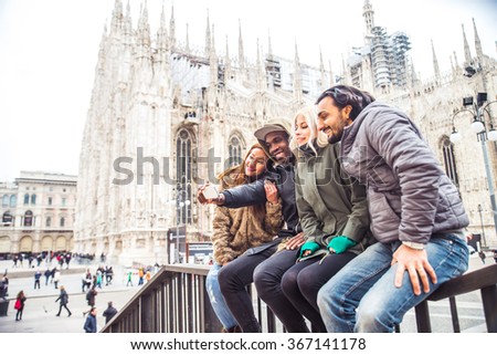 Multiethnic group of friends taking a selfie with smart phone to share on a social network - people of diverse ethnic having fun outdoors, Milan\'s Duomo cathedral in the background