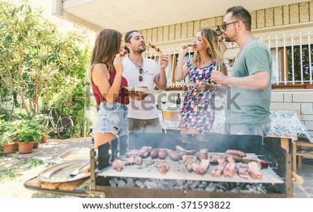 Group of friends making barbecue outdoor in their countryside house. Cooking, eating and spending time with good mood
