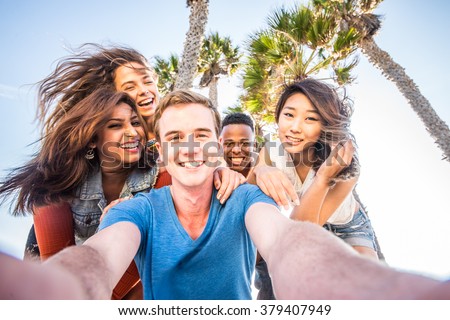 Multi-ethnic group of friends taking a self portrait picture with a camera phone - Cheerful people of diverse ethnics having fun and partying outdoors on a summer vacation
