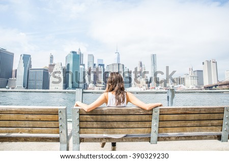 Woman sitting on a bench and looking at New York skyline - Tourist enjoys the view of Manhattan cityscape