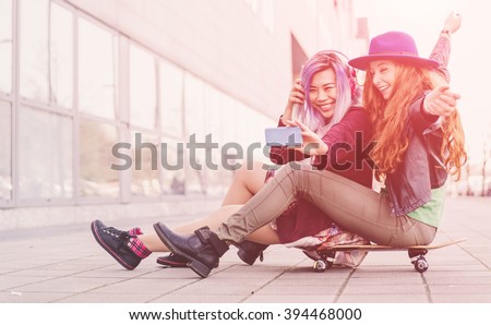 Two teen girls taking selfie sitting on a skateboard