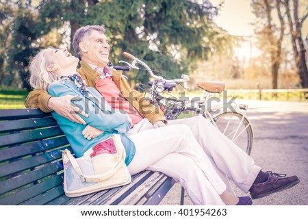 Senior cheerful couple sitting on a bench in a park - Two pensioners having fun together outdoors
