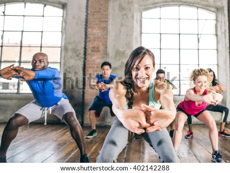 Multi-ethnic group of people training in a gym - Trainer and sportive persons doing squats in a fitness class