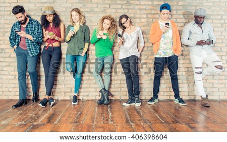 Young people looking down at cellular phone - Teenagers leaning on a wall and texting with their smartphones - Concepts about technology and global communication