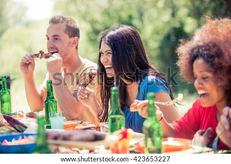 Multicultural group of friends grilling and having party in the backyard - Barbecue outdoors, people eating while talking and laughing