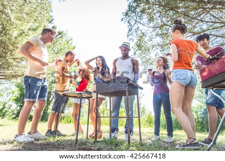 Group of friends having fun at barbecue party outdoors - People grilling, dancing and drinking wine