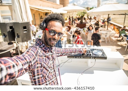 Dj taking a selfie while mixing music on a deejay set in a club, people dancing