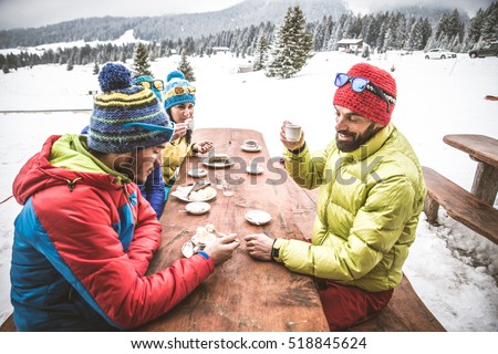 Group of friends talking and having fun in a outdoor restaurant on winter holidays - Snowboarders drinking hot coffee in a bar