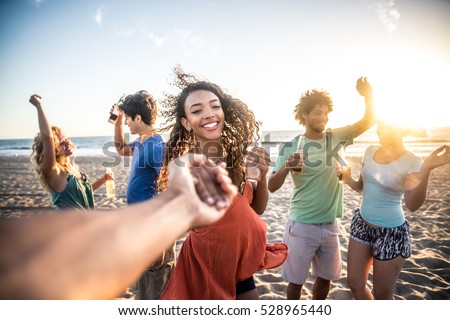 Multi-ethnic group of friends partying on the beach at sunset, pov prospective - Woman taking his boyfriend to dance