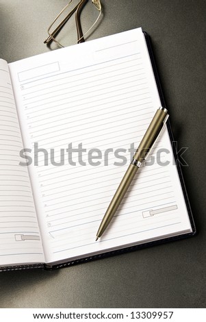 The notebook and glasses with the pen lays on a grey background