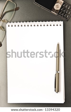 The notebook and cellular phone with the pen lays on a grey background