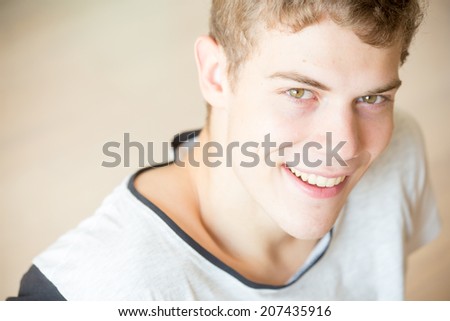 A young blonde male model is smiling attractively into the camera with a simple background