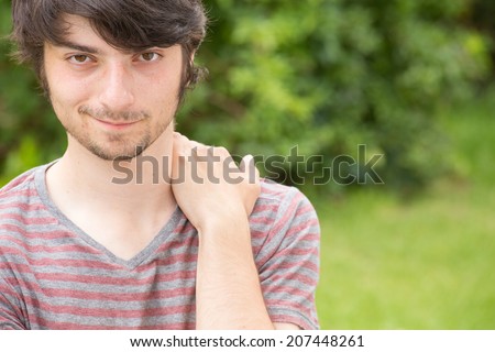 A young male model is looking attractively into the camera while holding his back