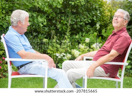 Two elderly men are sitting together enjoying the day with a nice talk - the right one is looking up