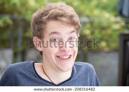 A young blonde male model is smiling into the camera and raising his eyebrows with a nice modern background