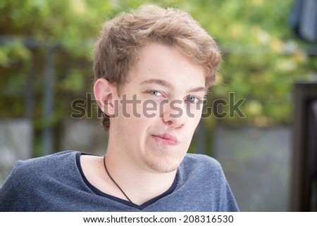 A young blonde male model is looking straight at the camera seriously and distorting his mouth.
