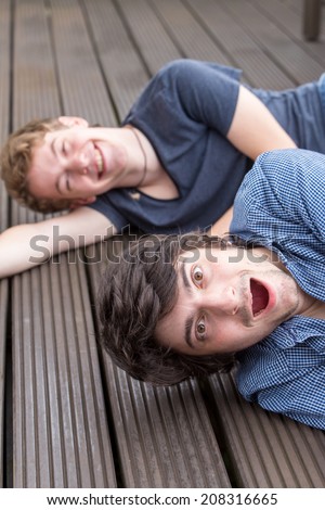 Two young male models are lying on the ground, laughing and having a lot of fun. The front model is very surprised while the one behind is lying on the ground and laughs