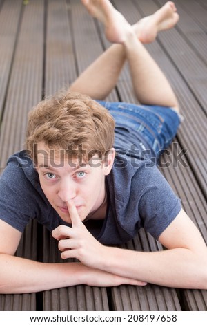 A young blonde male model is picking his nose in a funny way