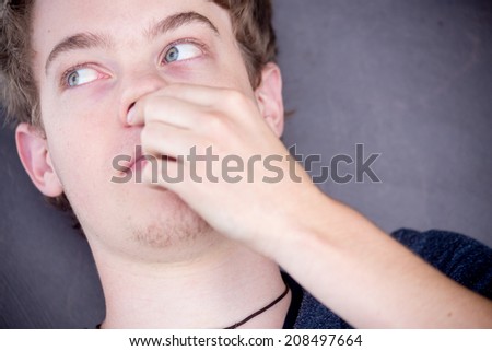 A young blonde male model is touching his nose with a nice modern grey background