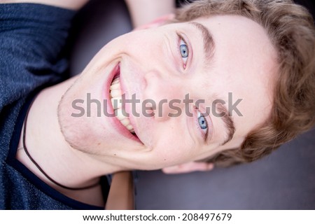 A young blonde male model is smiling in an evil manner into the camera with bright blue eyes and is happy