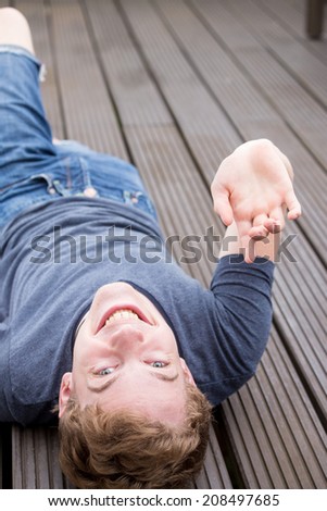 A young blonde male model is lying on his back and laughing