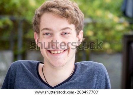 A young blonde male model is smiling into the camera with a nice modern background - left