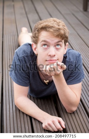 A young blonde male model is lying on the ground and thinking