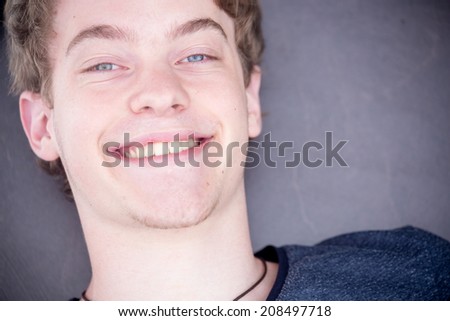 A young blonde male model is smiling into the camera and raising his eyebrows with a nice modern grey background