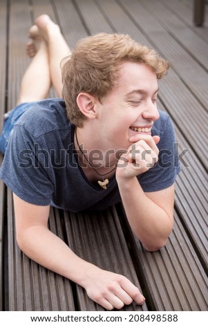 A young blonde male model is lying on the ground and laughing