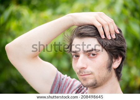 A young male model is brushing through his hair attractively and looking into the you