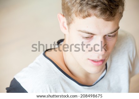 A young blonde male model is looking down and thinking with a simple background