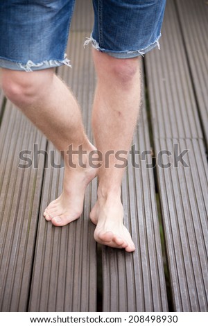 Beautiful bare feet from a young male model are walking on dark wooden planks, one feet lifted