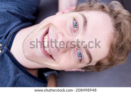 A young blonde male model is smiling in an evil manner into the camera with bright blue eyes and intense eyes