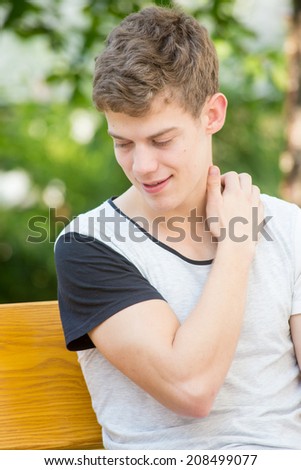 A young male model is reaching for his back with closed eyes in an attractive fashion