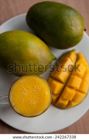 Top view of fresh mango smoothie and ripe mangoes on the white plate