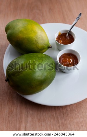 Two small dishes of fresh mango chutney with ripe mangoes on white plate
