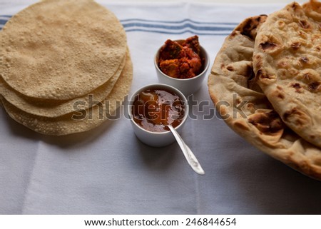 Fresh Indian flat breads nan and poppadom served with mango chutney and pickle on the table.