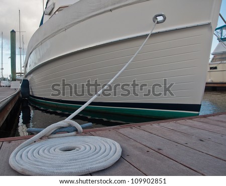 Dock cleat with a white line tied around it, then coiled beside the cleat.  boat secured to boat dock in background