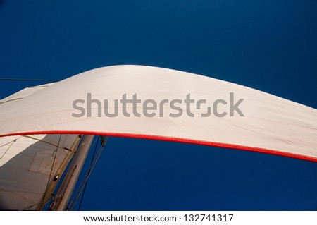 Cloudless blue sky with two white sails set.  Main sail and jib sail with red trim. horizontal image with copy space