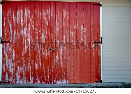 Faded red barn door with black latches on a white building
