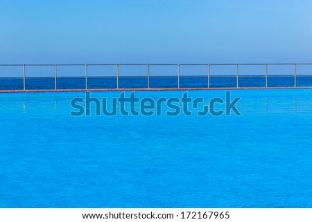 Swimming Pool Ocean Blue Swimming pool waters outdoor alongside beach coastline with blue ocean sea horizon.