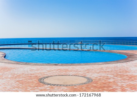 Swimming Pools Oceans  Blue swimming pool waters outdoor alongside beach coastline with ocean sea horizon.