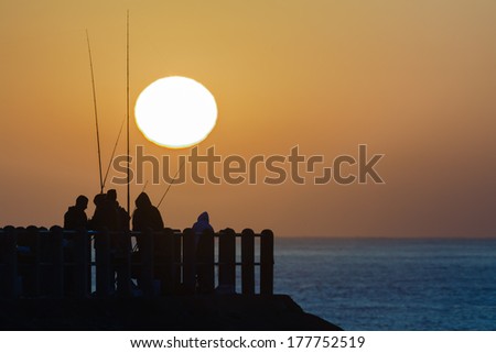 Dawn Sunrise Ocean Pier Fishing Dawn with sun rising over ocean sea waters with fishermen silhouettes on pier jetty.