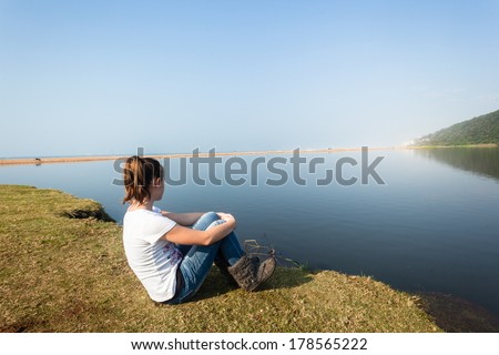 Girl Sitting River Water Lagoon Teen girl relax sitting by beach river lagoon waters on a calm blue day in the countryside