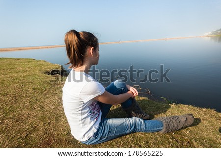 Girl Sitting River Water Lagoon Teen girl relaxing sitting by beach sea river lagoon waters on a calm blue day in the countryside