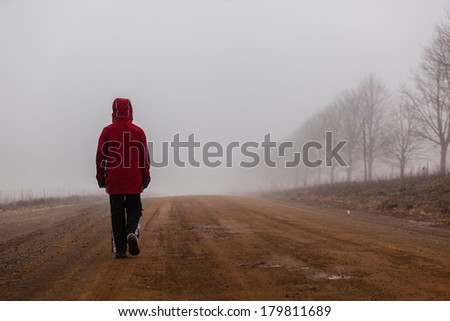 Teenager Dirt Road Mist Walking Teenager unidentified walking down mountain dirt road alone covered in cloud winter mist with color contrasts