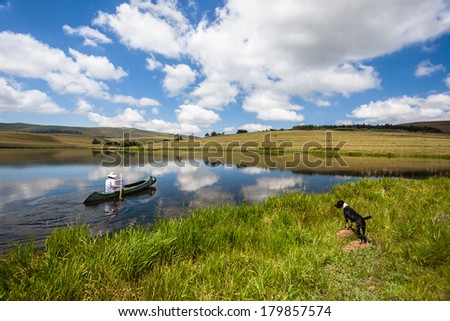 Woman Canoe Paddling Mirror Lake Reflections Woman paddling canoeÃ?Â on mountain lake with mirror reflecting clouds on water and observing dog along shoreline.