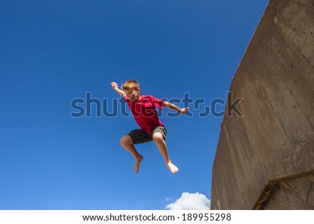 Teen Boy Jumping Blue Sky Teen boy jumping off wall against blue sky onto beach parkour