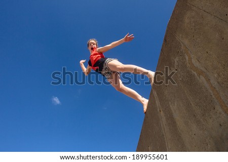 Girl Jumping Blue Sky Teen girl jumping off wall against blue sky onto beach in park hour