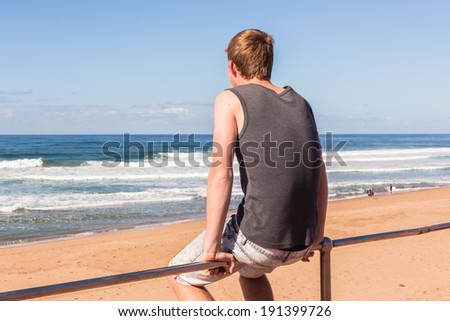 Boy Sitting Overlooking Ocean Waves Teen boy sitting on hand railing overlooking beach ocean waves landscape